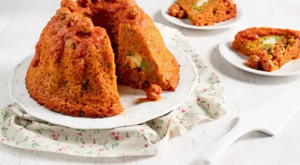 Sartu di riso, un tortino di riso rosso con polpettine e uova sode, servito su un piatto con tovagliolo fiorato.
