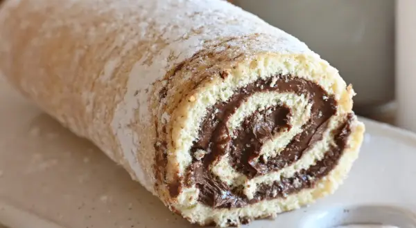Un soffice rotolo alla Nutella, cosparso di zucchero a velo, pronto per essere gustato.