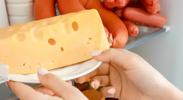 Mano che prende un pezzo di formaggio svizzero dal frigorifero, tra altri tipi di formaggio e insaccati.