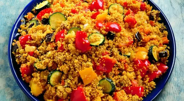 Un piatto colorato di cous cous con verdure miste: peperoni rossi e gialli, zucchine e melanzane.