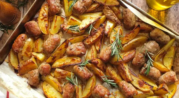 Salsiccia e patate al forno, dorate e profumate al rosmarino, su una teglia. Un piatto rustico e invitante.