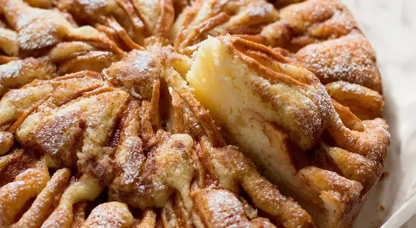 Una deliziosa torta di mele, cosparsa di zucchero a velo, con una fetta rimossa che rivela la morbida consistenza.
