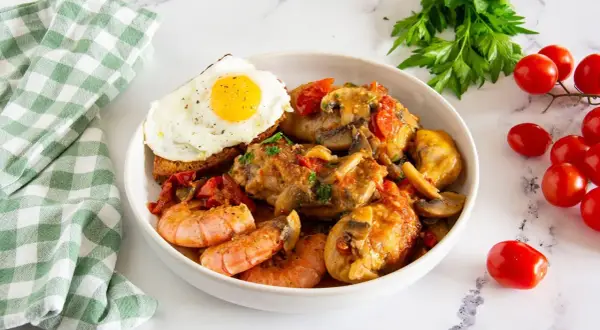 Un saporito pollo alla marengo con gamberi, funghi e pomodorini, servito con un uovo fritto su crostino.