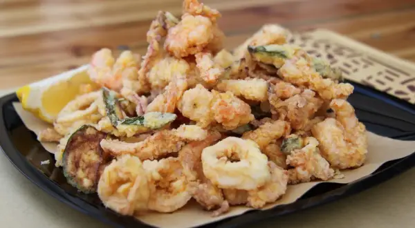 Un piatto invitante di frittura di pesce croccante, con gamberi, anelli di calamaro e verdure, accompagnato da uno spicchio di limone.