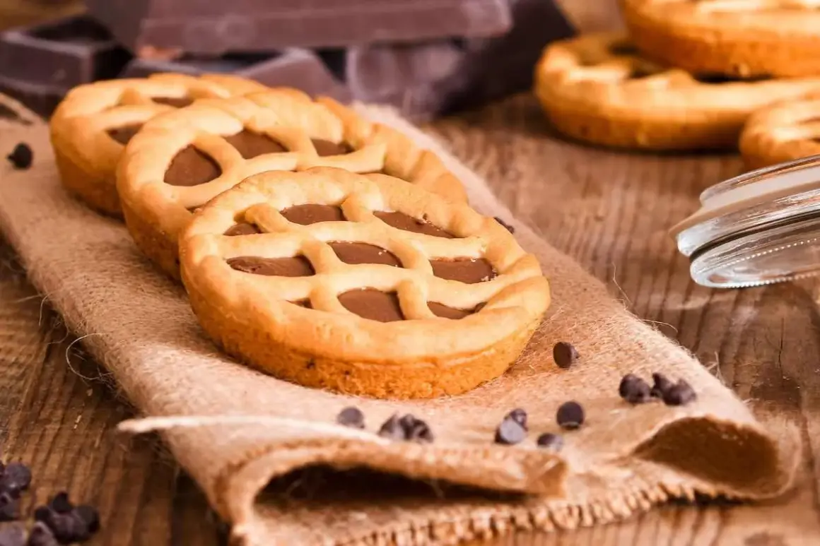 Deliziose crostatine al cioccolato con una griglia di pasta frolla dorata, su un sacco di juta, con gocce di cioccolato sparse.