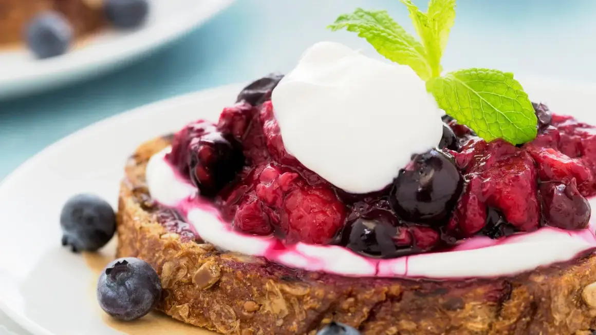 Fetta di pane integrale con yogurt greco, frutti di bosco e menta. Una deliziosa colazione con yogurt greco.