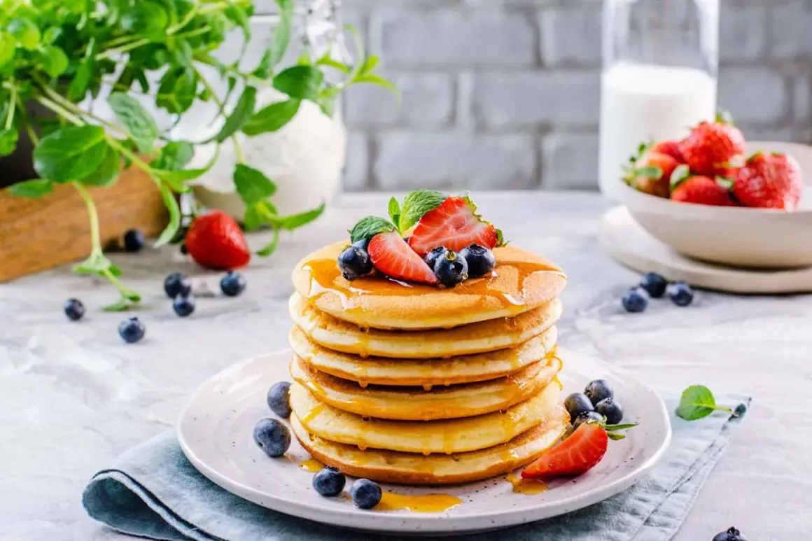 Pila di soffici pancake senza glutine, guarniti con fragole, mirtilli e sciroppo d'acero.