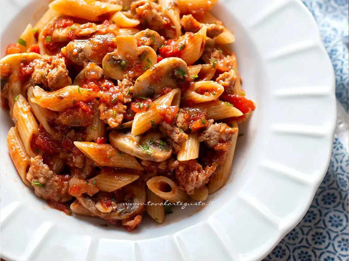 Piatto di pasta alla boscaiola con penne, funghi, salsiccia e pomodoro, condita con prezzemolo fresco.