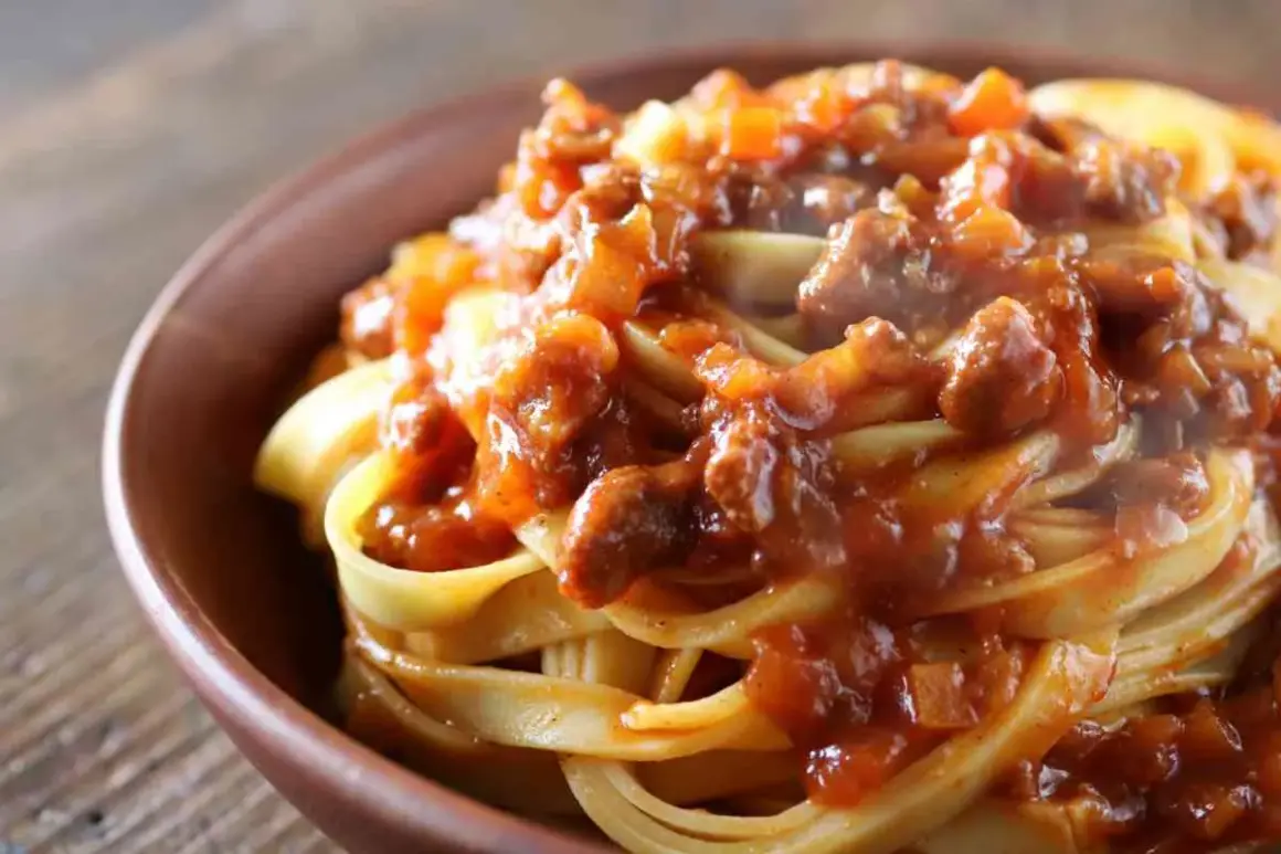 Tagliatelle al ragù, un classico dei primi piatti di carne, servite in una ciotola di terracotta.