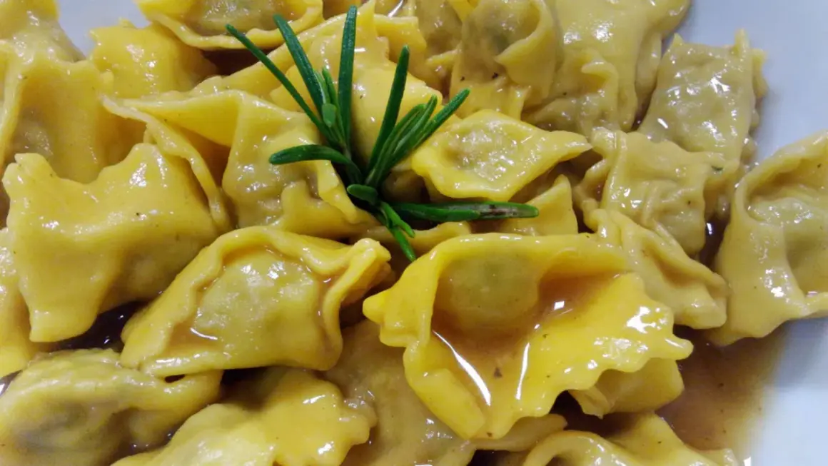 Un piatto invitante di ravioli del plin, conditi con un sugo dorato e guarniti con un rametto di rosmarino fresco.