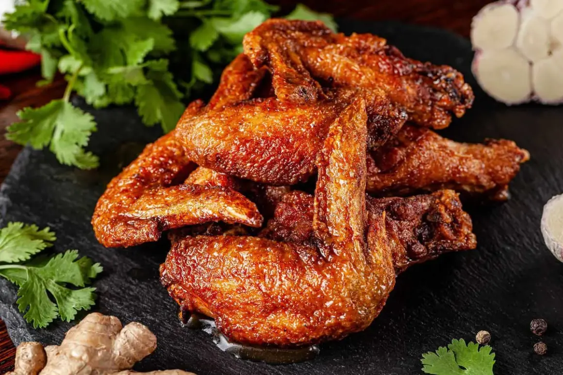Alette di pollo dorate e succulente, servite su una pietra scura con coriandolo fresco, zenzero e aglio.