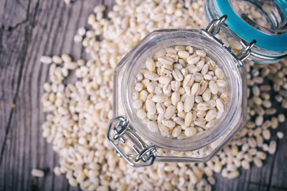 Orzo perlato in un barattolo di vetro, circondato da chicchi sparsi. Attenzione, l'orzo fa ingrassare se consumato in eccesso!
