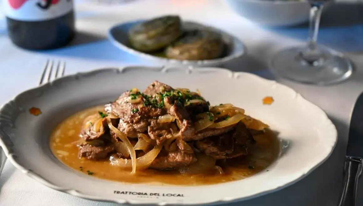 Fegato alla veneziana, un classico veneto, servito su un piatto bianco con cipolle caramellate e prezzemolo tritato.