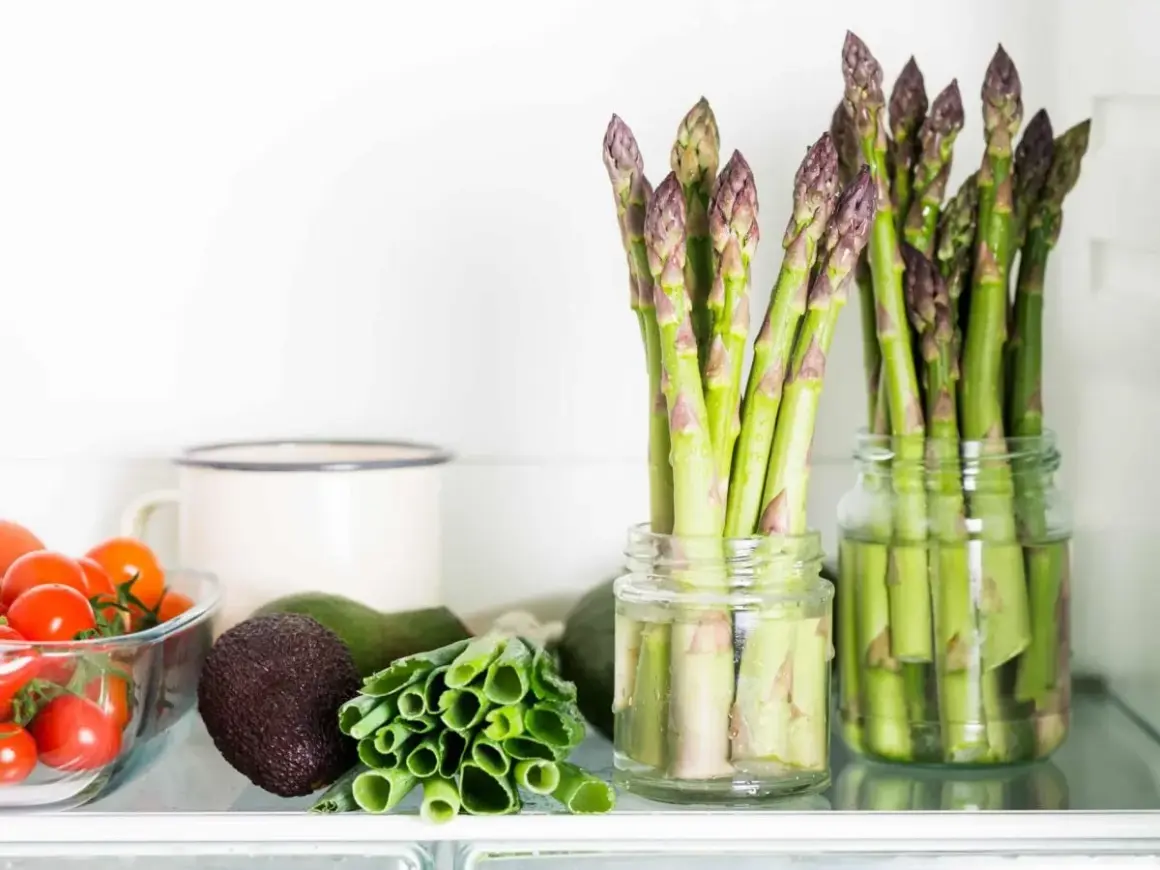 Asparagi freschi in barattoli con acqua, un ottimo modo per conservare gli asparagi. Vicino pomodorini, avocado e cipollotti.