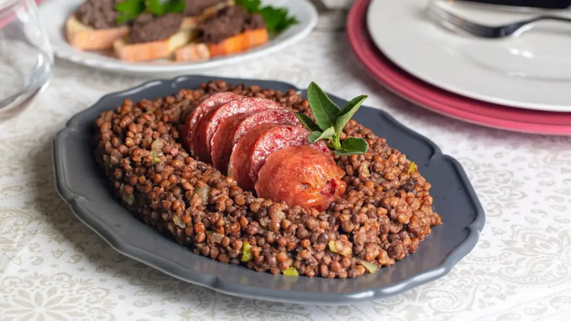 Piatto di lenticchie con fette di cotechino fresco, guarnito con una fogliolina di salvia.
