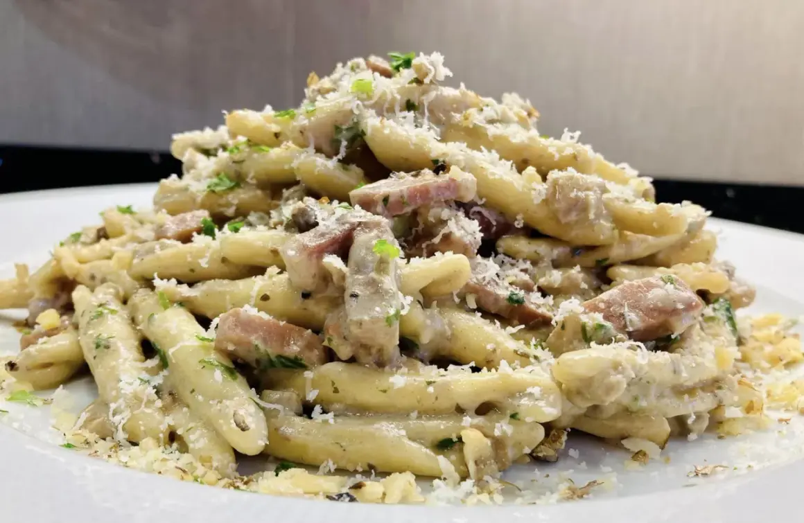 Un piatto invitante di pasta con speck, condita con una cremosa salsa, prezzemolo tritato e abbondante parmigiano grattugiato.