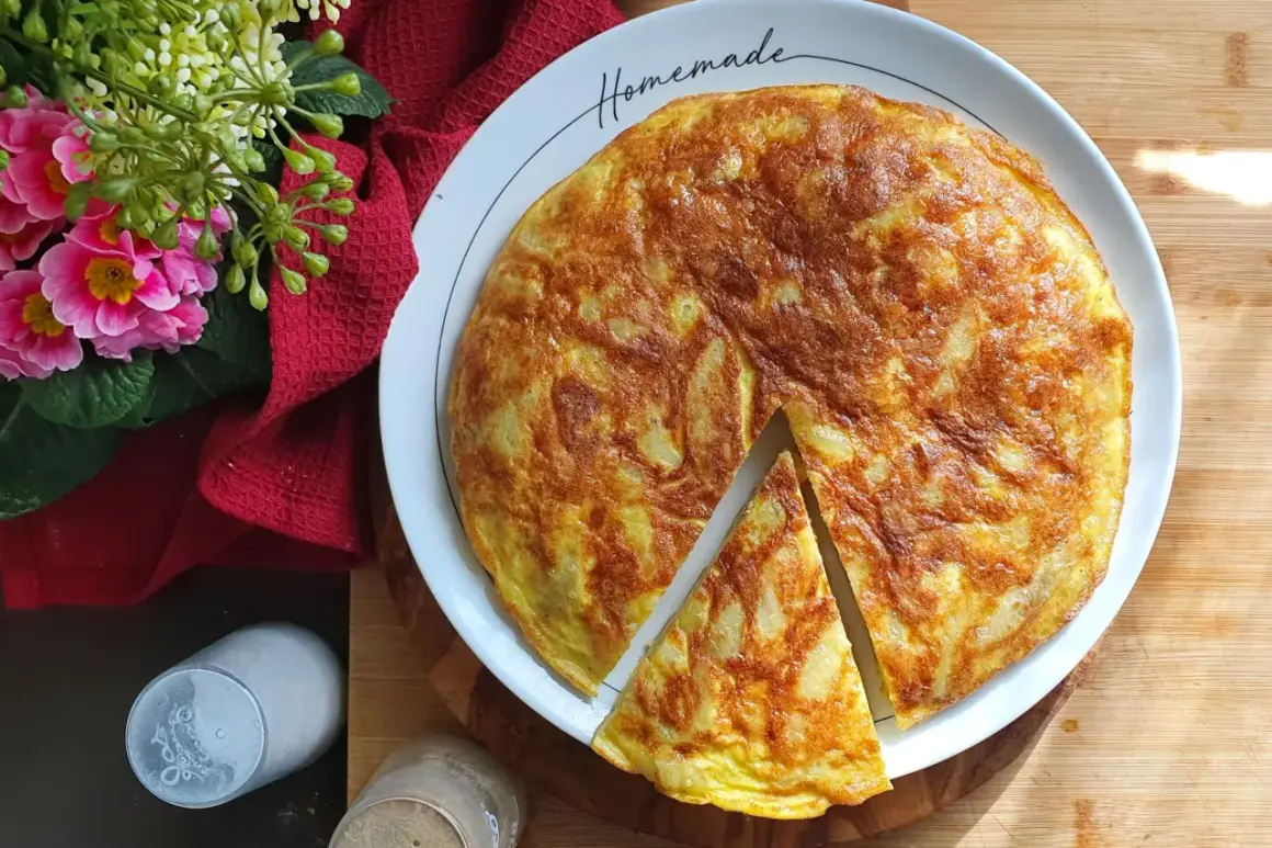 Una deliziosa frittata di patate fatta in casa, dorata e invitante, servita su un piatto bianco con fiori rosa e un tovagliolo rosso.