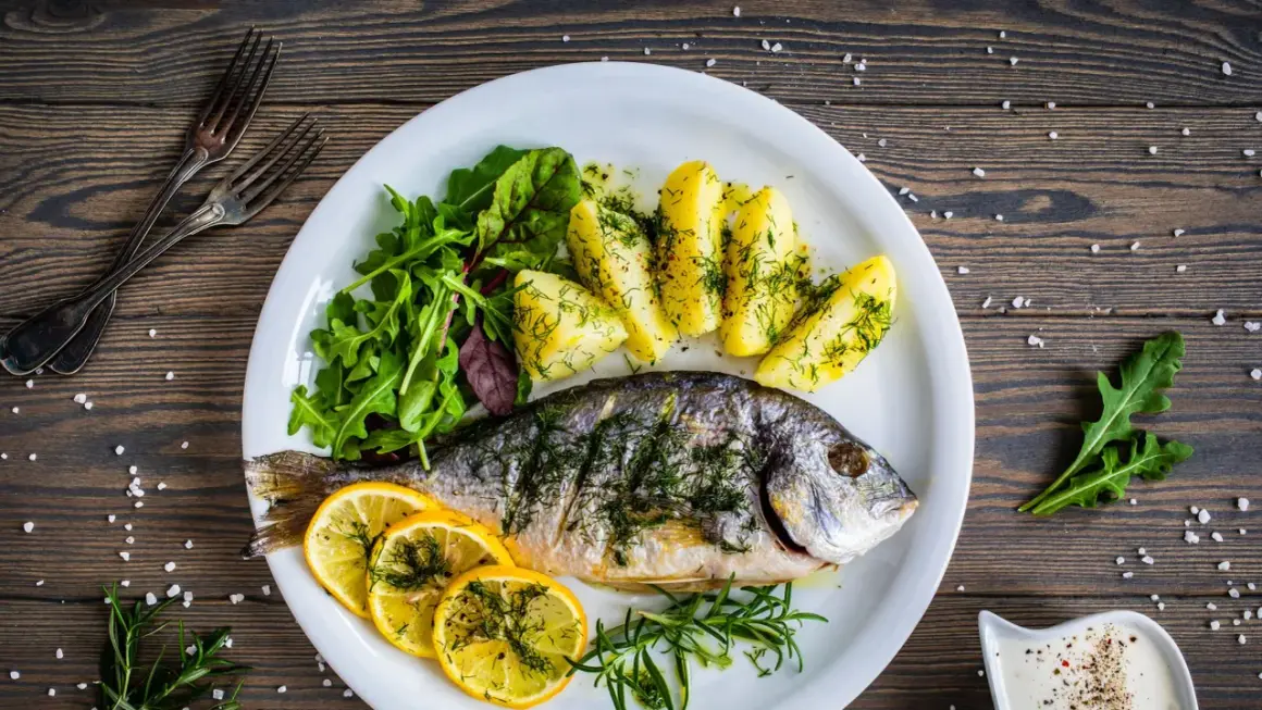 Orata in padella, cotta alla perfezione, servita con patate, limone e insalata fresca. Un piatto delizioso e salutare.