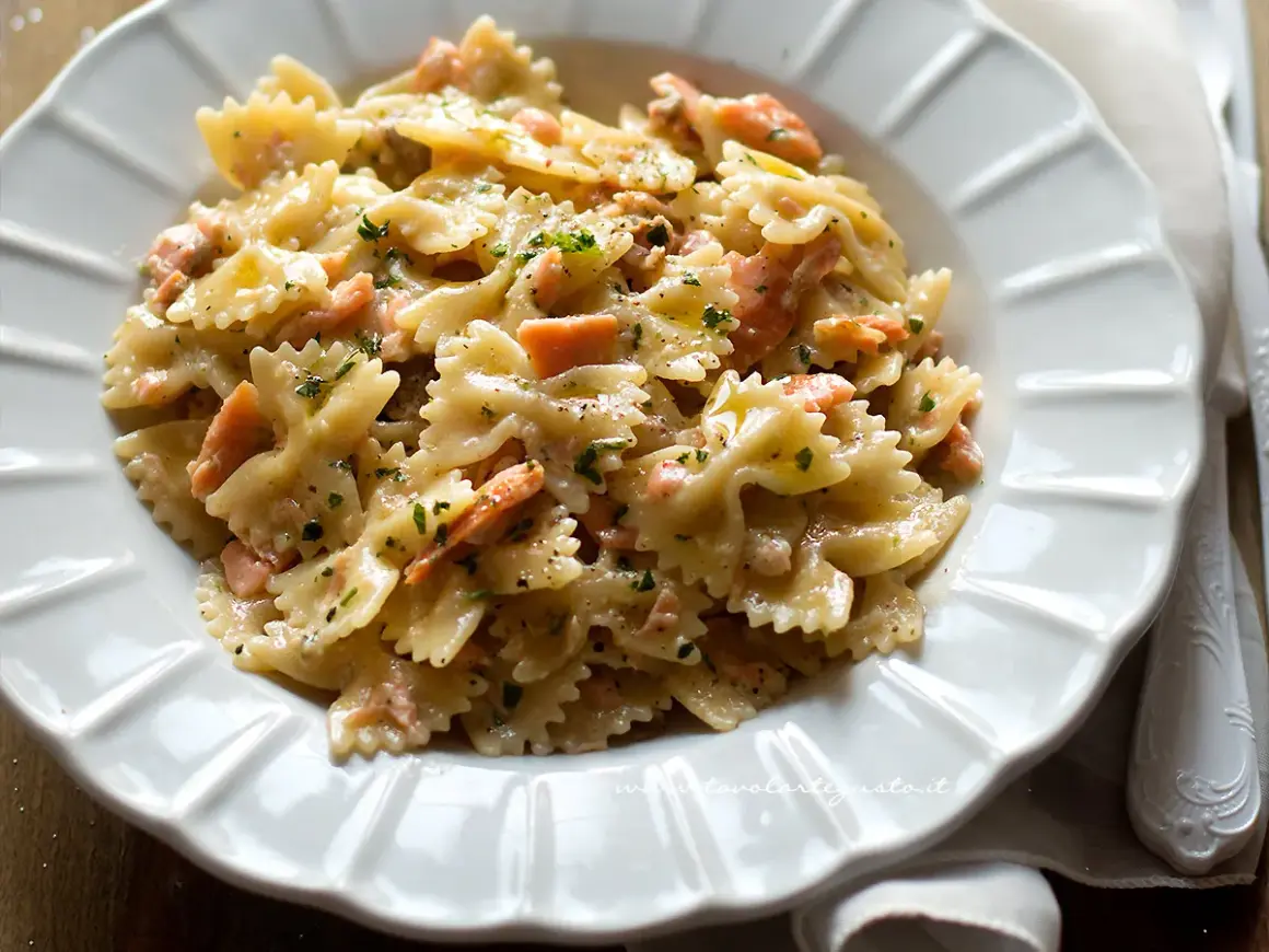 Farfalle cremose con pezzetti di salmone e prezzemolo tritato, un piatto invitante di pasta al salmone.