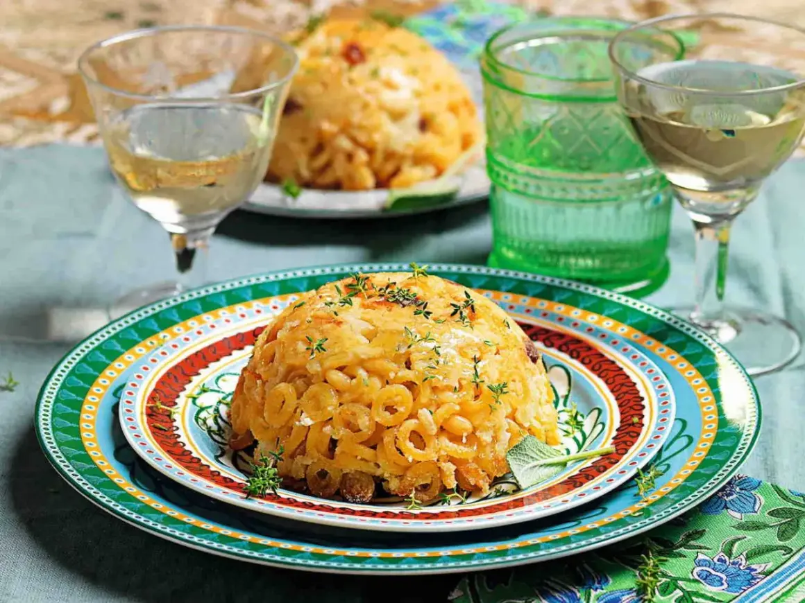 Anelletti al forno dorati e invitanti, guarniti con erbe aromatiche, serviti su piatti colorati con bicchieri di vino bianco.