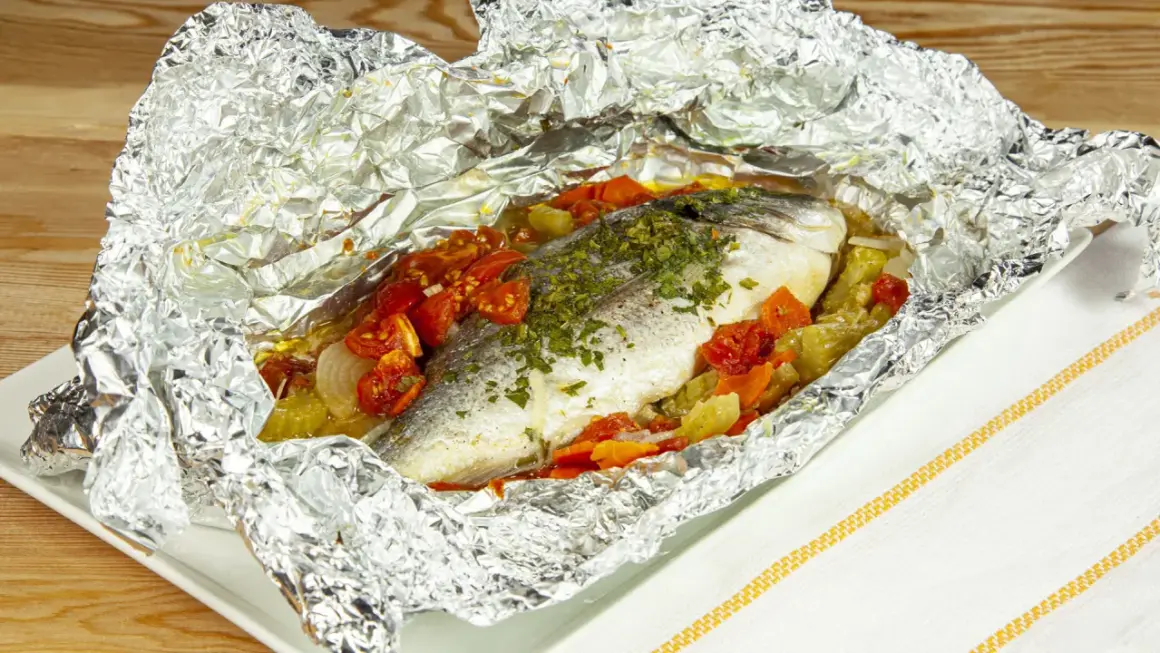 Orata al cartoccio con pomodorini e verdure, cotta al forno in un involucro di alluminio, pronta per essere gustata.