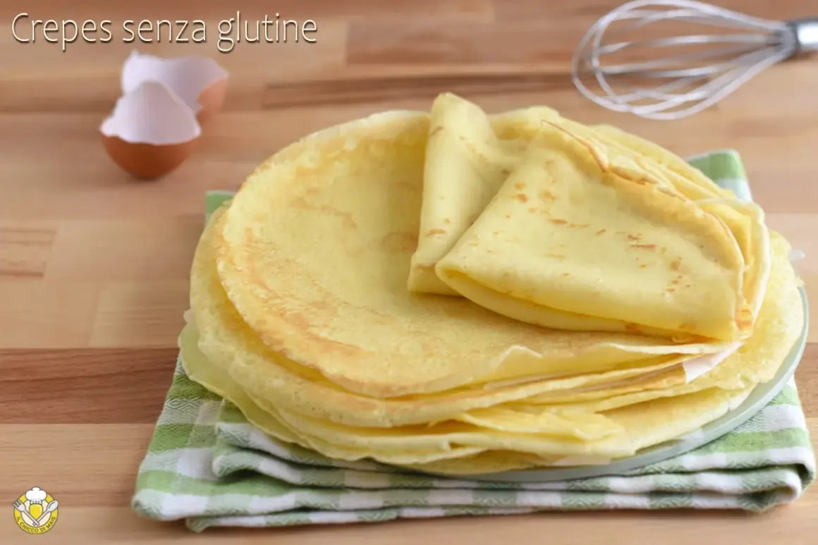 Pila di crepes senza glutine dorate e soffici, pronte per essere farcite. Sullo sfondo, gusci d'uovo e una frusta.