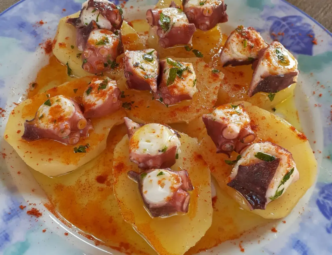 Un delizioso polpo alla gallega su patate, condito con paprika e prezzemolo, servito su un piatto blu e bianco.