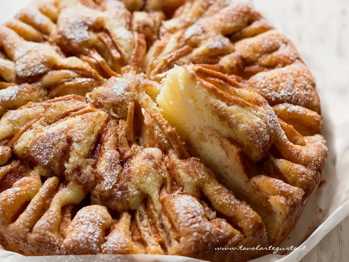Una deliziosa torta di mele, cosparsa di zucchero a velo, con una fetta rimossa che rivela la morbida consistenza.