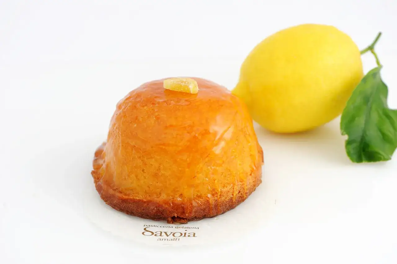 Delizia al limone lucida, con un limone fresco e una foglia verde sullo sfondo.