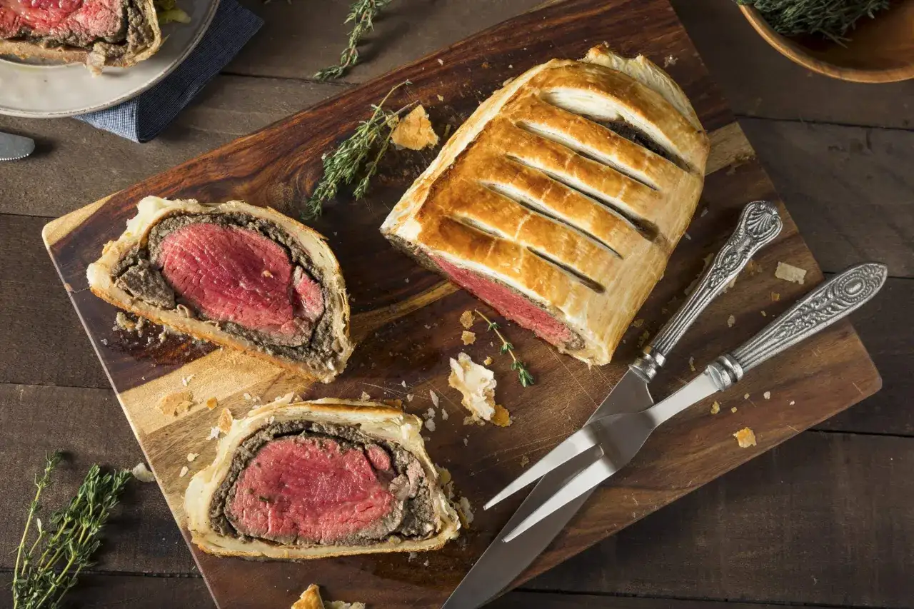 Un succulento filetto alla Wellington, tagliato per mostrare la carne rosata e la croccante sfoglia dorata, pronto per essere servito.