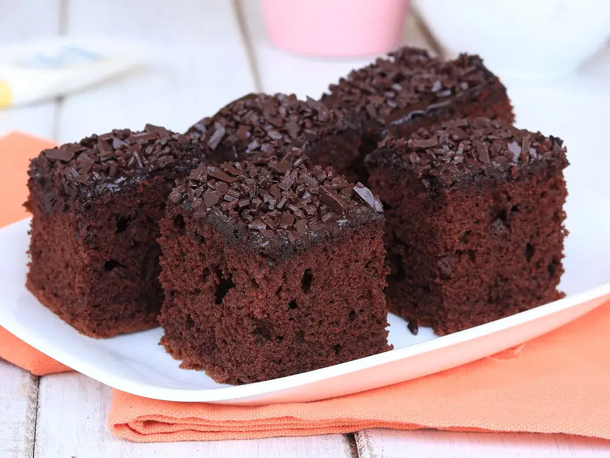 Quattro fette di torta al cioccolato, soffice e ricoperta di scaglie di cioccolato, su un piatto bianco con tovagliolo arancione.