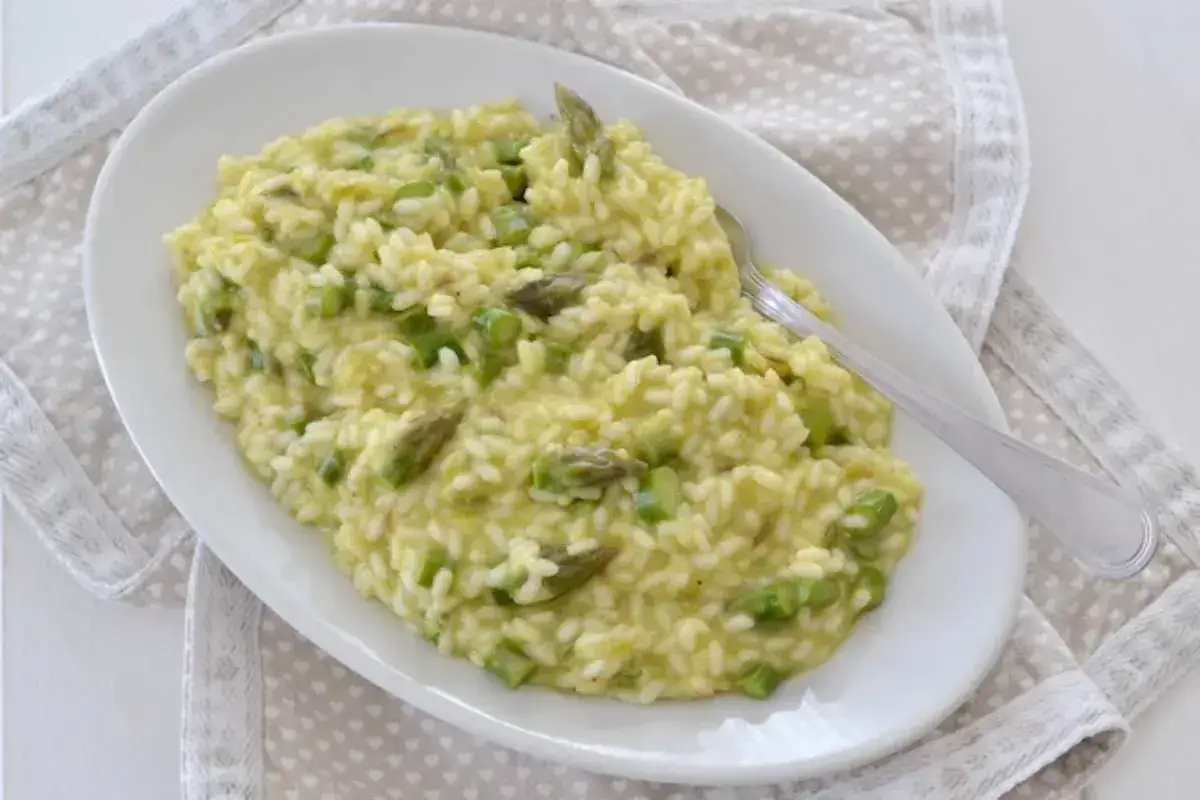 Un cremoso risotto con asparagi, servito su un piatto ovale bianco, con una forchetta argentata appoggiata sopra.