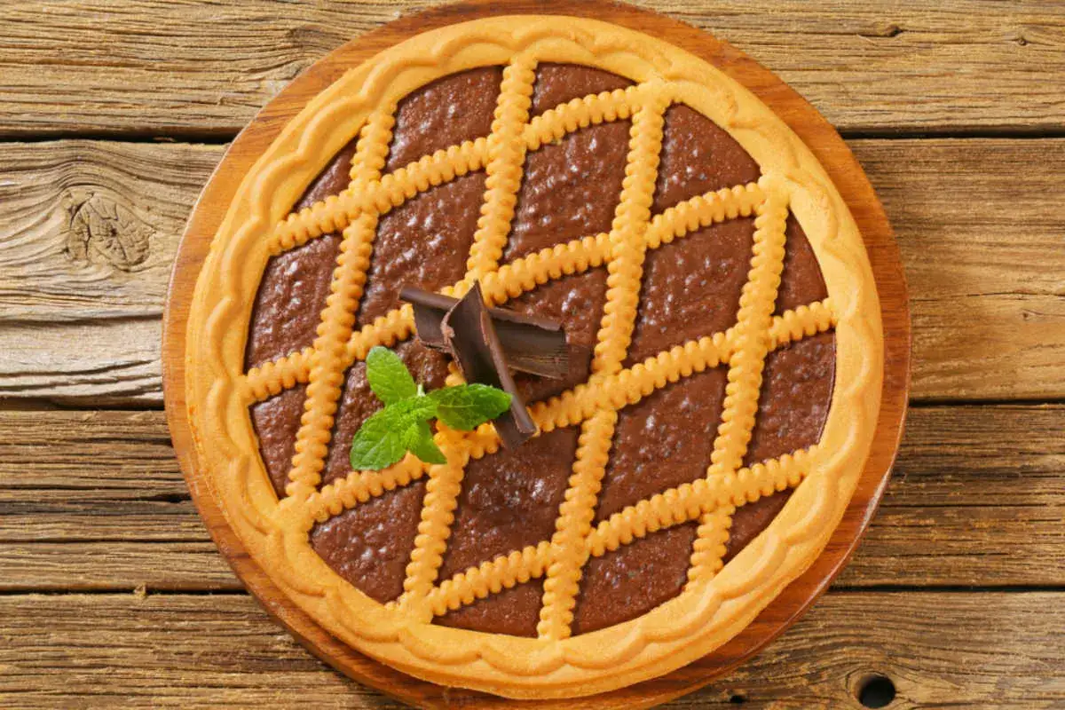 Deliziosa crostata al cioccolato con decorazione a griglia, guarnita con scaglie di cioccolato e foglioline di menta.