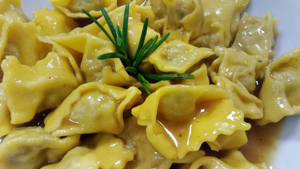 Un primo piatto invitante: ravioli del plin dorati, conditi con un sugo saporito e guarniti da un rametto di rosmarino fresco.