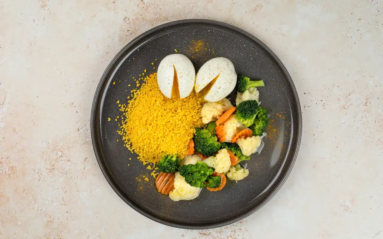 Piatto di cous cous con verdure miste, broccoli, cavolfiori e carote, accompagnato da due uova sode tagliate a met&agrave;.