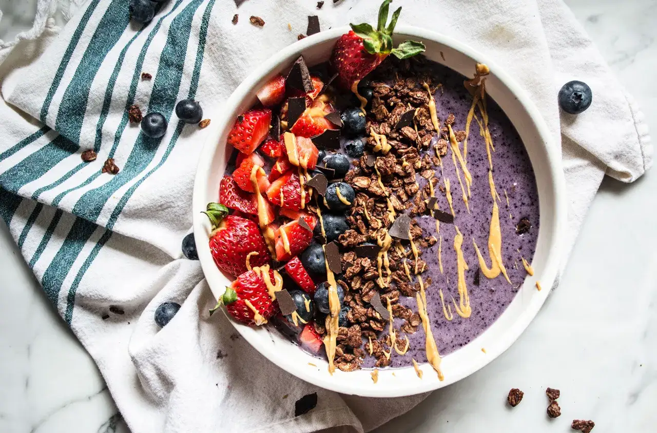 Ciotola con smoothie viola, fragole, mirtilli, granola e cioccolato. Un'opzione salutare di frutta con meno zuccheri.