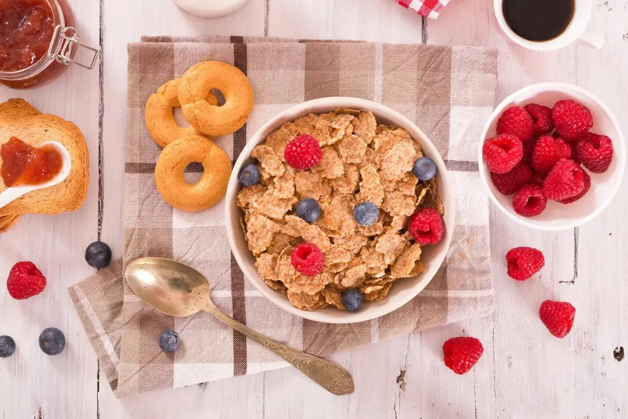 Una deliziosa colazione senza glutine con fiocchi di cereali, lamponi, mirtilli, biscotti e marmellata.
