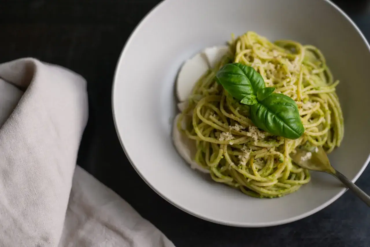 Un piatto di linguine al pesto, guarnito con basilico fresco e parmigiano, servito con mozzarella.
