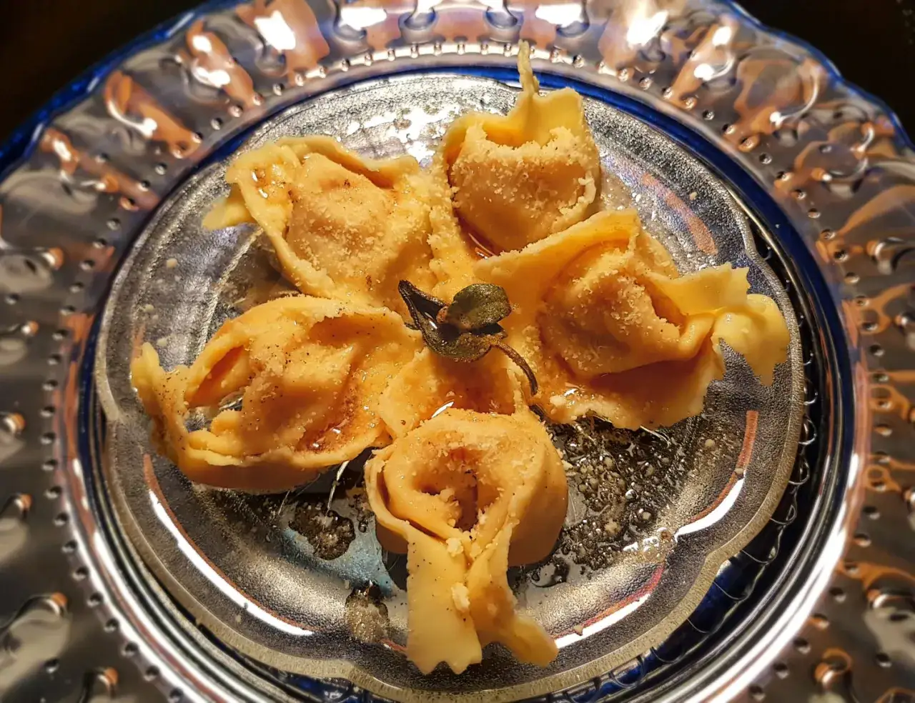 Tortelli di zucca dorati, spolverati di parmigiano, su un piatto decorato. Un tocco di salvia completa questo piatto.