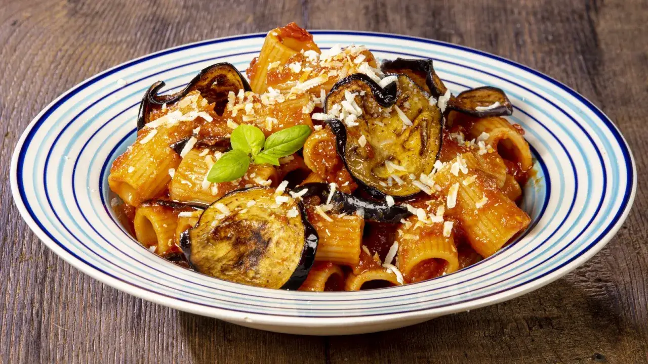 Un piatto invitante di mezze maniche alla norma, con melanzane fritte, sugo di pomodoro e ricotta salata grattugiata.