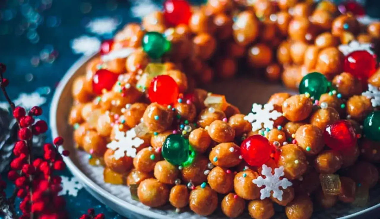 Struffoli ricetta napoletana: palline dorate glassate, decorate con ciliegie rosse e verdi, fiocchi di neve e zuccherini colorati.