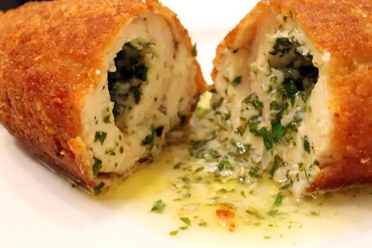 Pollo alla kiev succulento, tagliato a met&agrave;, con ripieno cremoso e erbe aromatiche. Burro fuso cola sul piatto.