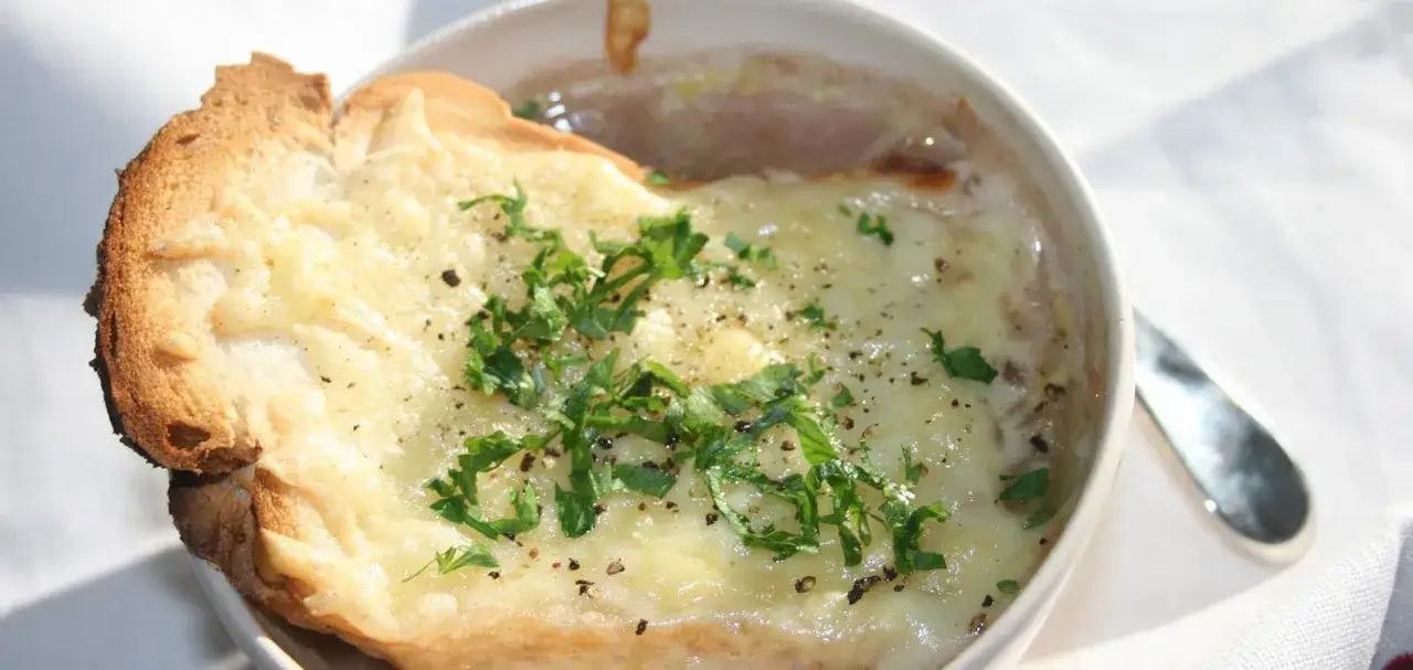 Una ciotola di zuppa di cipolle fumante, ricoperta di formaggio fuso e crostini dorati, guarnita con prezzemolo fresco.