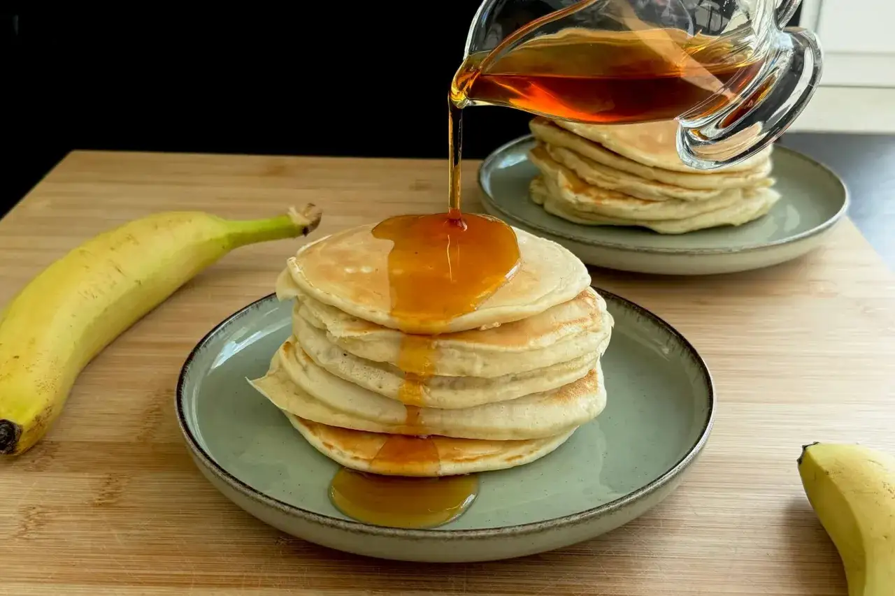 Pancake alla banana con sciroppo d'acero che cola su una pila di soffici pancake.