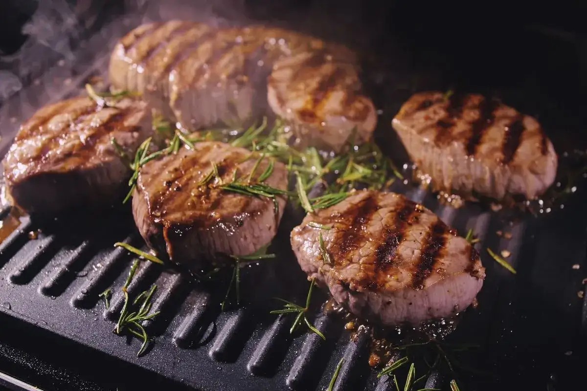 Succulenta carne da fare alla brace, con rosmarino e fumo che sale, su una piastra calda.