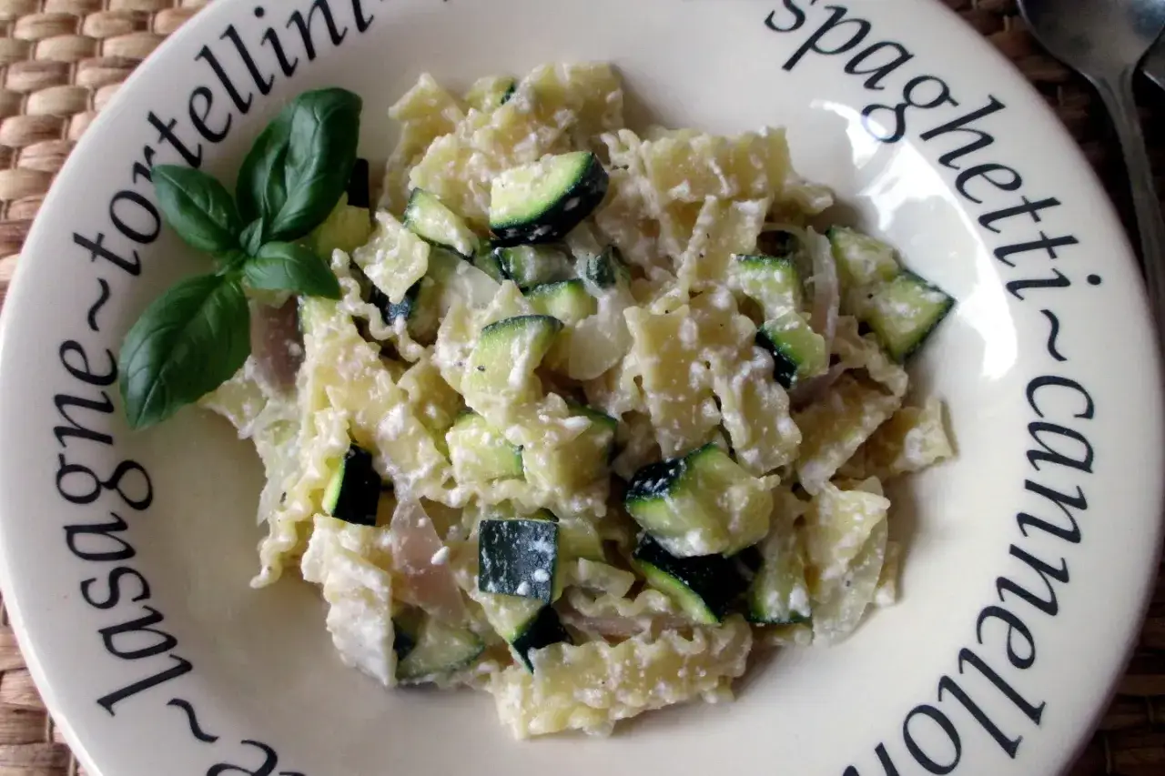 Piatto di pasta con zucchine e ricotta, guarnito con basilico fresco. Un primo piatto leggero e gustoso.