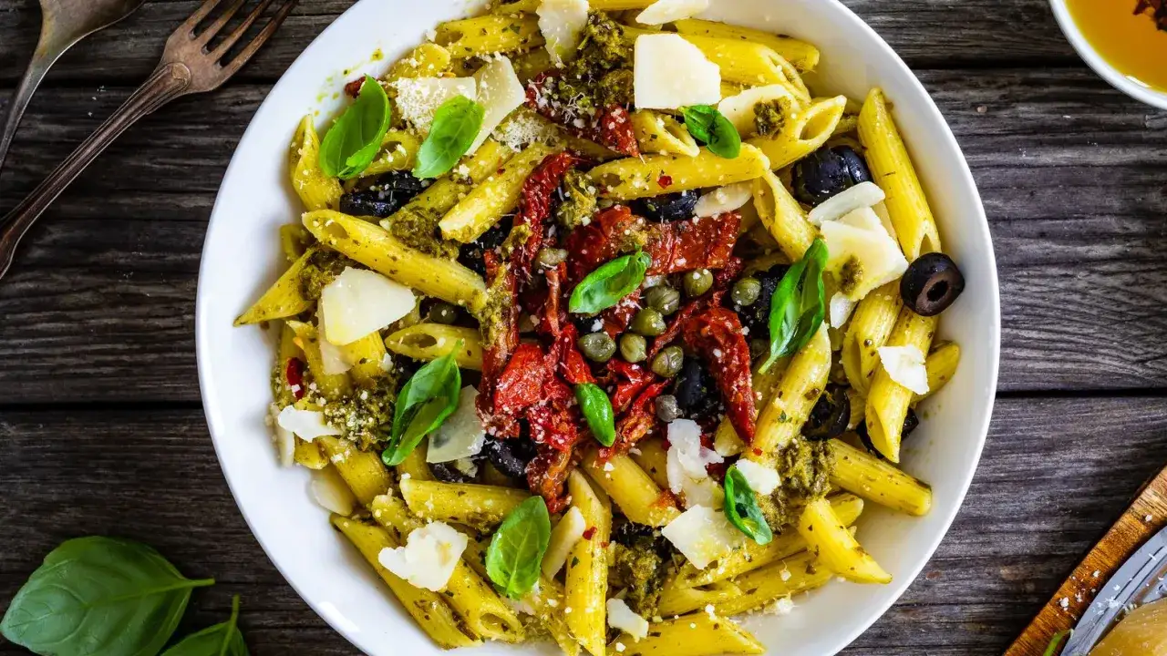 Penne al pesto con pomodori secchi in busta, olive, capperi e scaglie di parmigiano. Un piatto gustoso e facile da preparare.