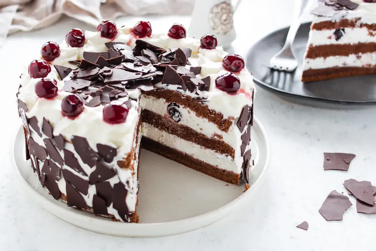 Una fetta di foresta nera torta, con strati di cioccolato e panna, decorata con ciliegie e scaglie di cioccolato.