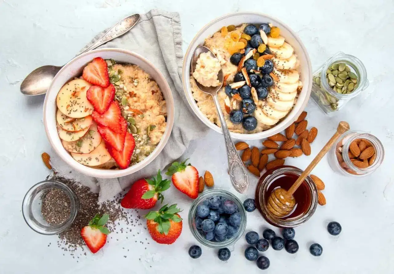 Due ciotole di fiocchi d'avena, una con fragole e mele, l'altra con mirtilli e banane. Perfetti per scoprire come mangiare i fiocchi d'avena in modo gustoso.