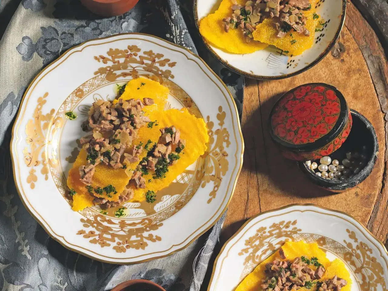 Piatto di fegato alla veneziana su polenta gialla, guarnito con prezzemolo tritato, servito su eleganti piatti con decorazioni dorate.
